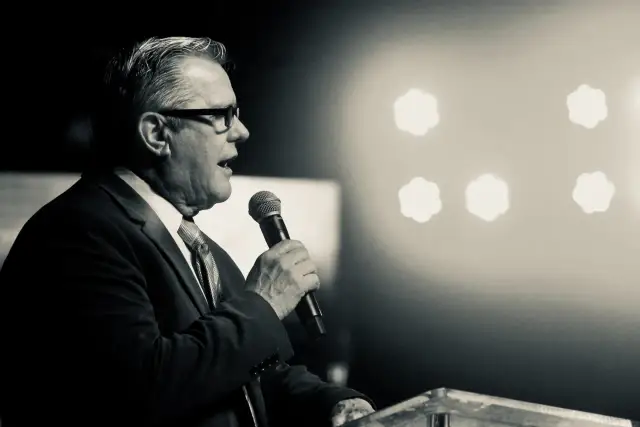 Mężczyzna w garniturze przemawia do mikrofonu. Jego motywacja do pracy płynie z chęci dzielenia się wiedzą i inspirowania innych.