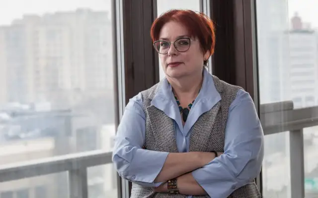 Kobieta w okularach, z rudymi włosami, opiera się o okno. Jej postawa sugeruje siłę i determinację w odpowiedzi na pytanie, jak żyć po rozwodzie.