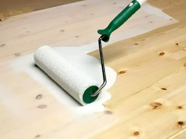 Wałek malarski rozprowadza białą farbę, nadając drewnianej podłodze efekt bielenia.