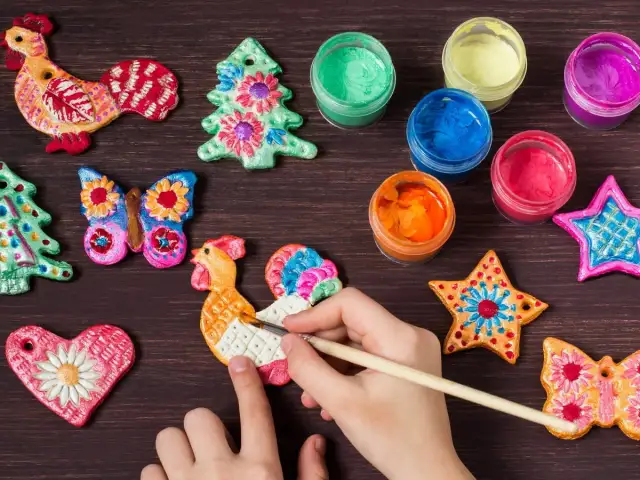 Dziecko maluje kolorowe ozdoby z masy solnej: koguty, choinki, gwiazdki i motyle.