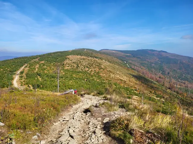Kamienista ścieżka na Skrzyczne. Czy to szlak zielony czy niebieski? W tle górzysty krajobraz z lasami i wieżą.