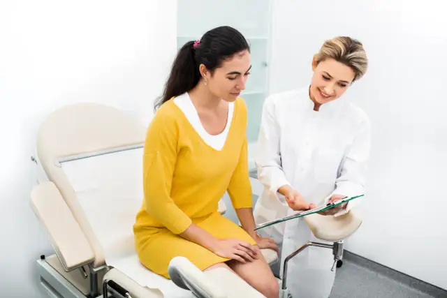 Lekarka w białym fartuchu pokazuje pacjentce wyniki badań na tablecie.