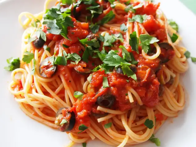 Pyszne spaghetti puttanesca przepis: makaron z sosem pomidorowym, oliwkami i natką pietruszki.