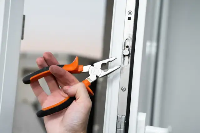 Dłoń z kombinerkami reguluje mechanizm okna, przygotowując je do trybu zimowego.