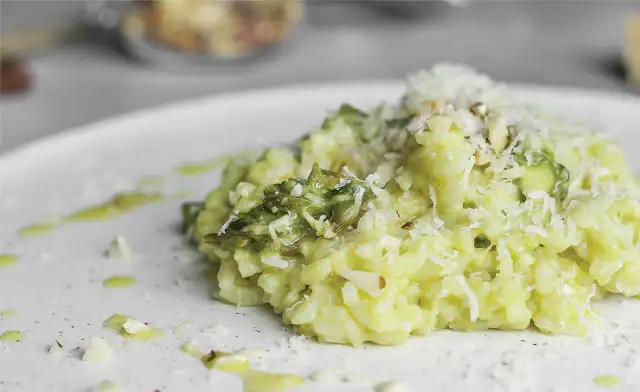 Kremowe risotto ze szparagami, posypane parmezanem i migdałami, na białym talerzu.