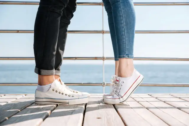 Para na drewnianym pomoście, w białych trampkach i jeansach. Idealne converse stylizacje damskie na letni dzień nad morzem.