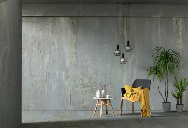 Beton architektoniczny w nowoczesnym wnętrzu. Krzesło z żółtym kocem, stolik z dzbankiem i filiżanką, rośliny.