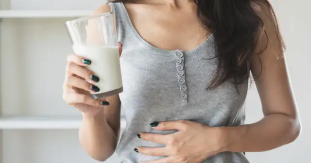 Kobieta z bólem brzucha trzyma szklankę napoju, zastanawiając się, czy mleko sojowe ma laktozę.