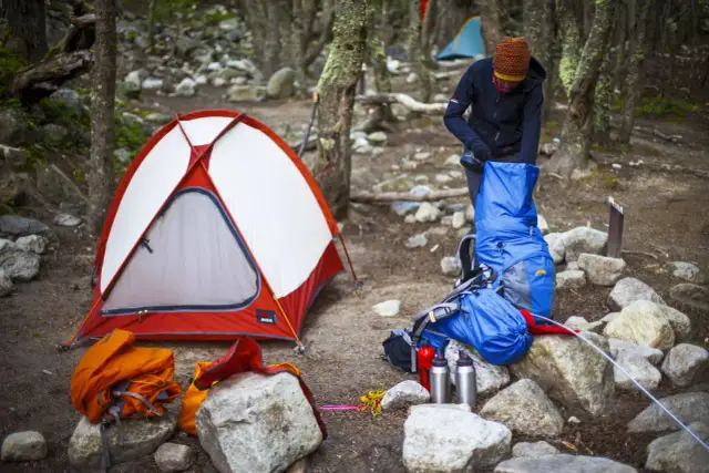 Osoba pakuje plecak obok namiotu. Warto wiedzieć, jak zabezpieczyć namiot przed deszczem, by biwak był udany.