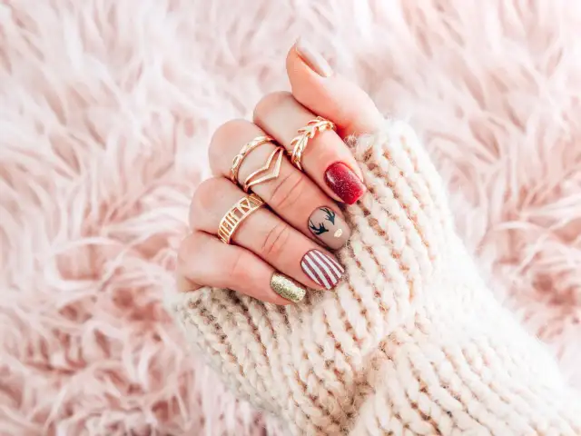 Festliche nägel zu weihnachten mit Rentier-Motiv, roten und goldenen Akzenten, umgeben von einem kuscheligen Strickpullover.