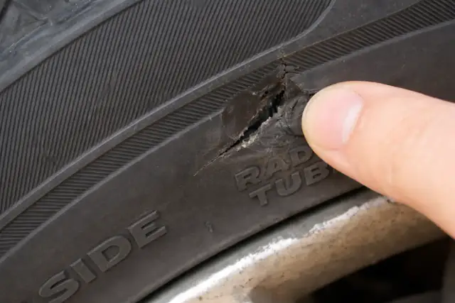 Palec wskazuje na pęknięcie bocznej części opony, które wymaga naprawy.