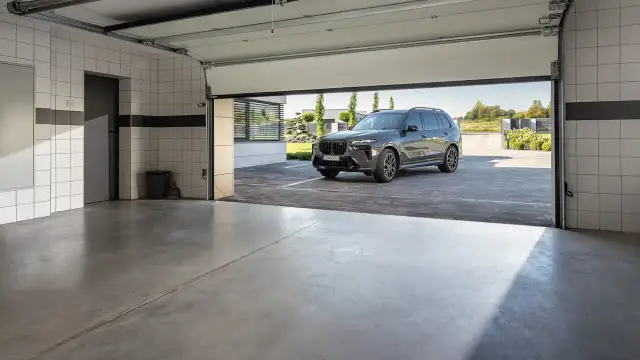 Nowoczesny garaż z betonową posadzką, idealny na jaki beton na posadzkę w garażu. Ciemny SUV czeka przed wejściem.