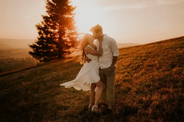 Romantyczna sesja zdjęciowa dla par na tle zachodzącego słońca. Para całuje się na wzgórzu, otoczona złotym światłem i naturą.
