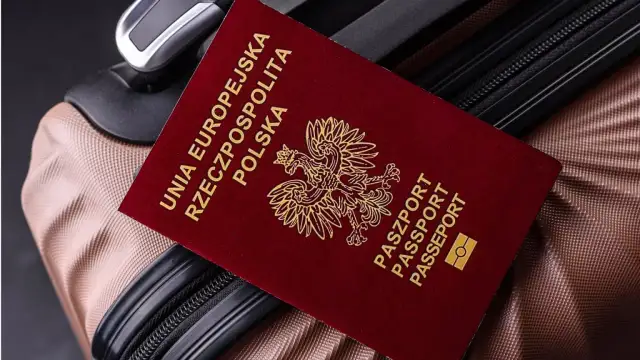 Czerwony paszport Polski z godłem orła leży na brązowej walizce.