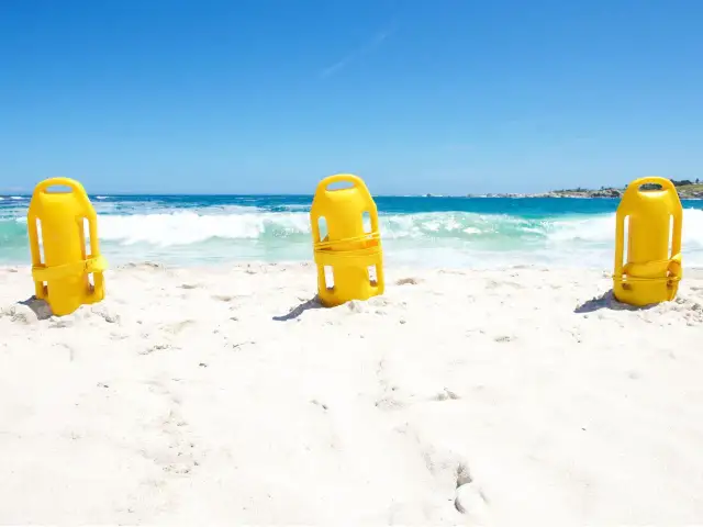 Trzy żółte bojki ratownicze stoją na piaszczystej plaży, z morzem i niebem w tle.
