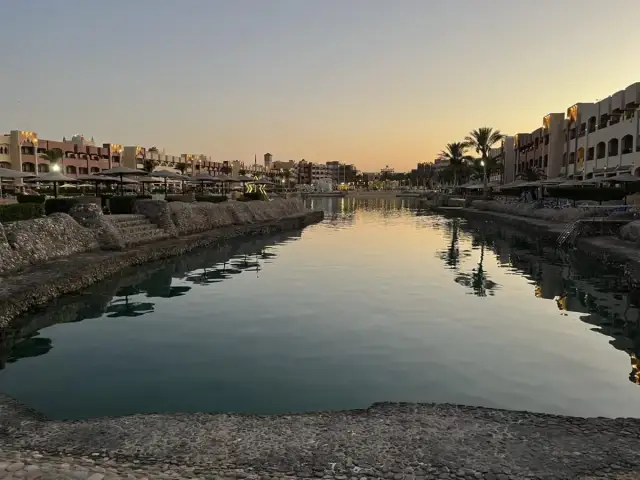 Zachód słońca nad kanałem w Hurghadzie z hotelami i palmami w tle.