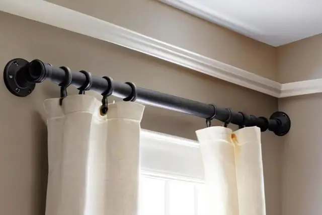 Czarny, industrialny karnisz do sufitu lub ściany, zamontowany nad oknem, z białymi zasłonami.