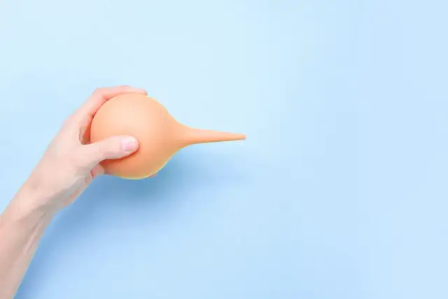 Dłoń trzyma pomarańczową gruszkę irygacyjną, która może być używana do lewatywy przed porodem.