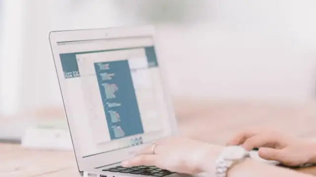 Dłonie piszące na laptopie, na ekranie widoczny jest fragment strony z tekstem.