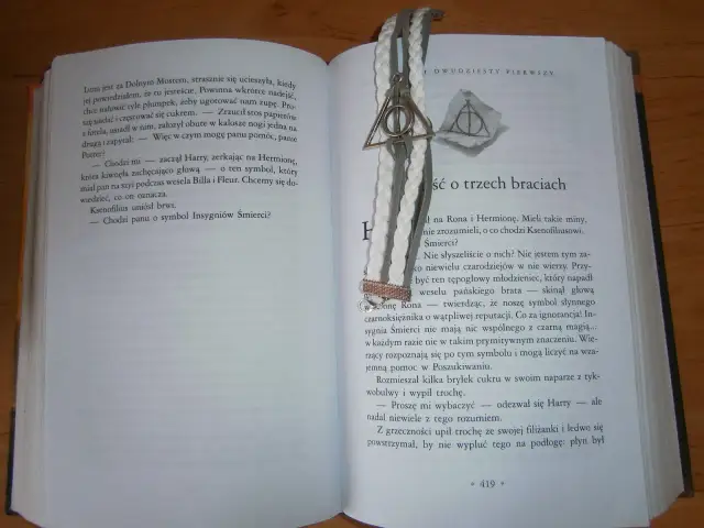 Otwarta książka z zakładką w kształcie symbolu Insygniów Śmierci. Tekst opowiada baśń o trzech braciach.