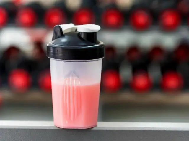 Przezroczysty shaker z różowym napojem na tle czerwonych kółek.