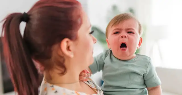 Płacz dziecka, być może z powodu objawów RSV, w ramionach mamy.