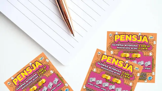 Zdrapki "Pensja" z nagrodą główną 3500 zł miesięcznie przez 2 lata, obok notatnika i długopisu.