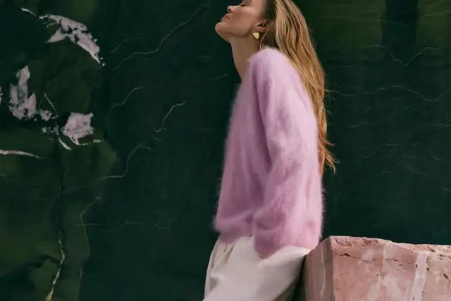 Kaszmirowy sweter w kolorze pudrowego różu otula ciało, dowodząc, czy kaszmir jest ciepły. Modelka w beżowych spodniach.