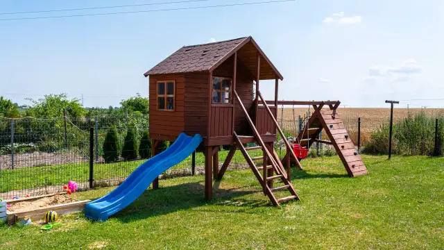 Drewniany domek na placu zabaw ze zjeżdżalnią, huśtawką i piaskownicą.