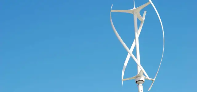 Biały wiatrak na dachu, z zakrzywionymi łopatami, obraca się na tle błękitnego nieba.