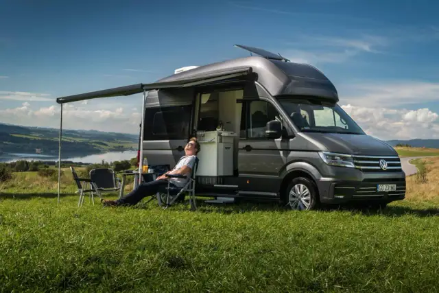 Mężczyzna odpoczywa przy kamperze VW California. Wymiary tego pojazdu pozwalają na komfortowe podróżowanie i biwakowanie.