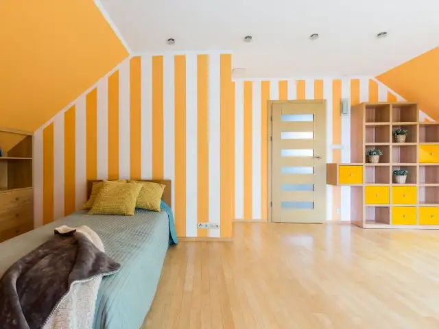 Pokój z łóżkiem i regałem, gdzie paski na ścianie pomysły dodają energii. Pomarańczowo-białe pasy na ścianie i suficie tworzą radosną atmosferę.