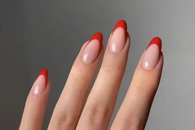 Dłonie z paznokciami w kształcie migdałków, ozdobione klasycznym french manicure z intensywnie czerwonymi końcówkami.