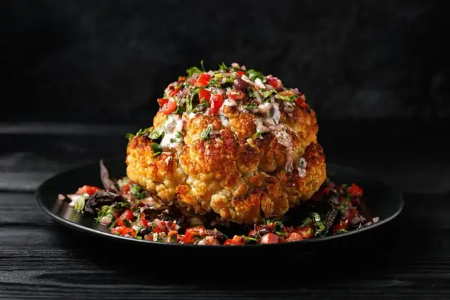 Ganz gebratener Blumenkohl mit Salsa und Sauce auf schwarzem Teller.