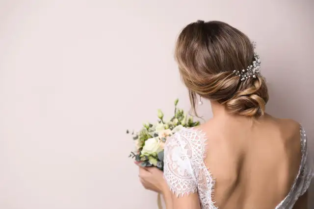 Elegancka panna młoda z bukietem kwiatów i ozdobną koroną na ślub, z tyłu głowy.