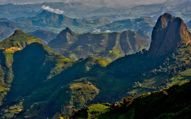 Zielone, pofałdowane góry Semien, oświetlone słońcem, z charakterystycznymi skalistymi szczytami i tarasowymi uprawami.