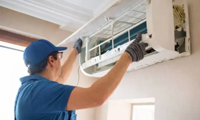 Fachowiec w niebieskiej czapce i rękawiczkach montuje klimatyzację w domu, dbając o każdy szczegół instalacji.