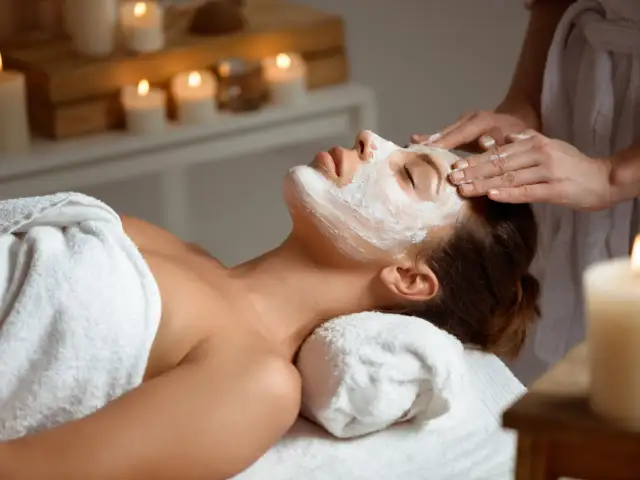 Kobieta z maską na twarzy podczas zabiegu w spa, w tle świece.