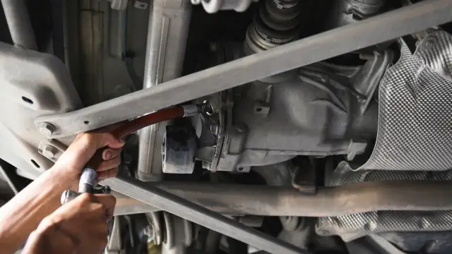 Wymiana oleju w tylnym moście. Mechanik używa wężyka do uzupełnienia płynu.