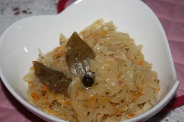 Pyszna kapusta kiszona zasmażana z liściem laurowym i zielem angielskim, podana w białej miseczce.