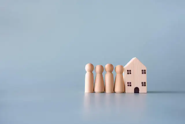 Drewniane figurki ludzi stoją obok domku. Symbolizują rodzinę i jej dom, pokazując, jak zachować mieszkanie przy upadłości.