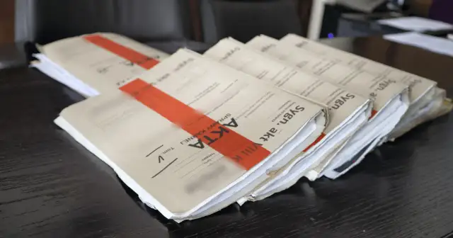 Stos akt sądowych z czerwonymi wstążkami na ciemnym drewnianym biurku.