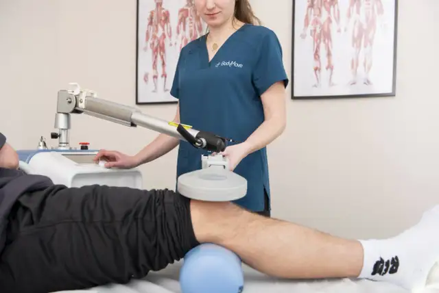 Fizjoterapeuta wykonuje zabieg rehabilitacyjny na kolanie pacjenta za pomocą specjalistycznego urządzenia.