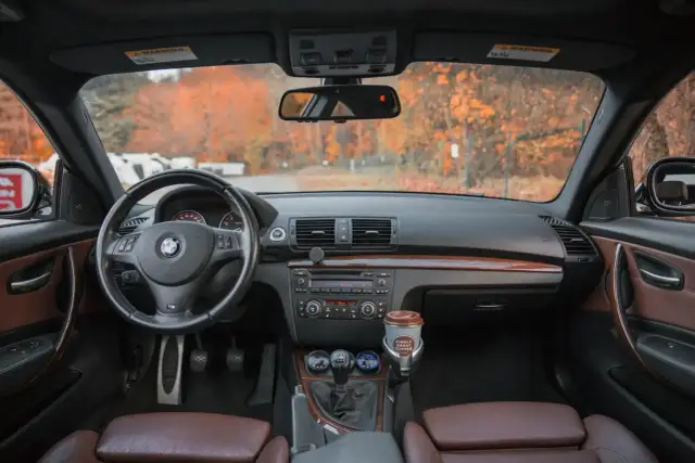 Wnętrze BMW z brązową tapicerką, kierownicą i panelem. Na desce rozdzielczej kubek kawy. Idealne miejsce na podpisanie umowy sprzedaży samochodu.