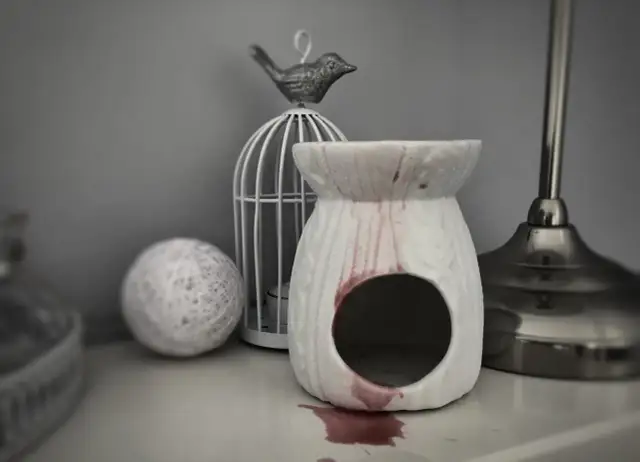 Biały kominek zapachowy z zaciekami wosku, obok klatka dla ptaków i kula z nici.