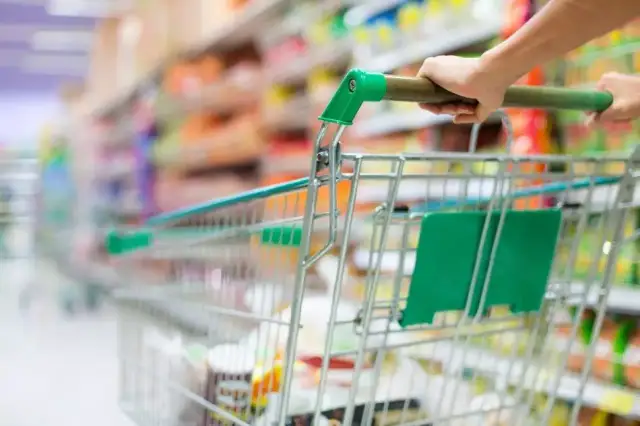 Ręka pcha wózek sklepowy w alejkach sklepu spożywczego, tworząc obraz dynamicznego doświadczenia w branży retail.