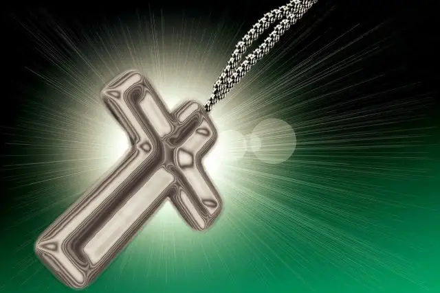 Metalowy krzyż na tle promieni światła i zieleni.