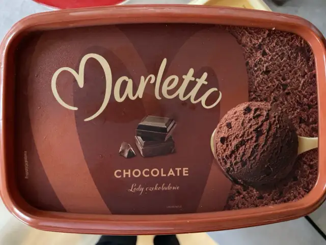Pudełko lodów czekoladowych Marletto z gałką lodów na łyżce i kawałkami czekolady.