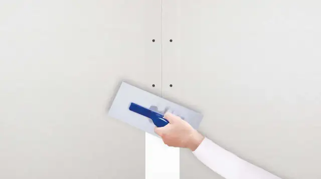 Ręka z kielnią nakłada gips szpachlowy na połączenie płyt gipsowo-kartonowych. Idealny do wygładzania i tworzenia równych powierzchni.