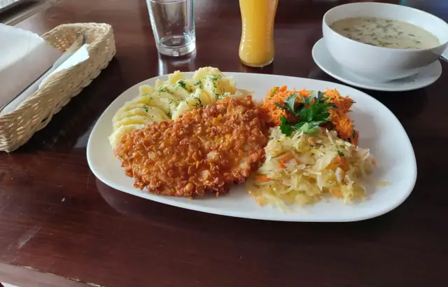 Talerz z panierowanym kotletem, ziemniakami, surówkami i zupą.